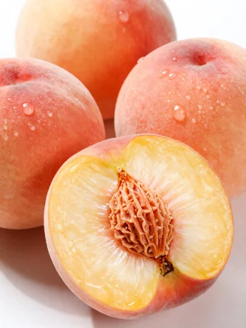 Celé a nakrájené broskve na dřevěném stole vedle sklenice broskvové šťávy